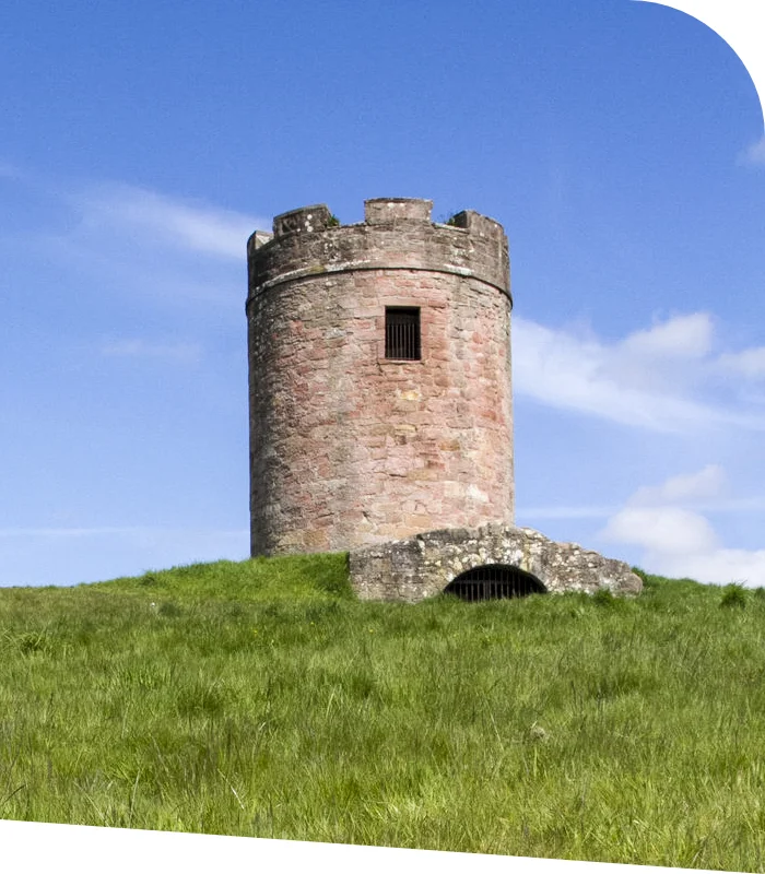 An old cylindrical stone tower with a crenelated top stands majestically on a grassy hill under a blue sky dotted with clouds, reminiscent of the timeless beauty that defines Clackmannshire accountants.