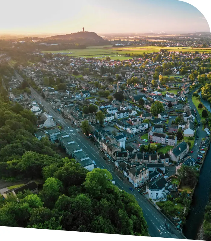 Aerial view of a town with a mix of residential buildings and greenery. A prominent hill and monument are visible in the background under a clear sky, reflecting the serene environment where Dunblane accountants offer their trusted services.