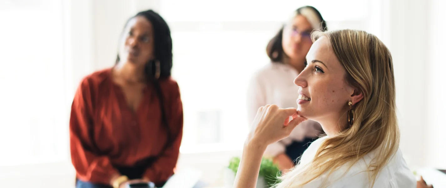 Aerial view of a riverside industrial site with solar-panel-topped buildings, various vehicles, and equipment scattered around. In the background, a bridge spans the river and mountains rise majestically, while some sustainable garden buildings add a touch of greenery to the scene.